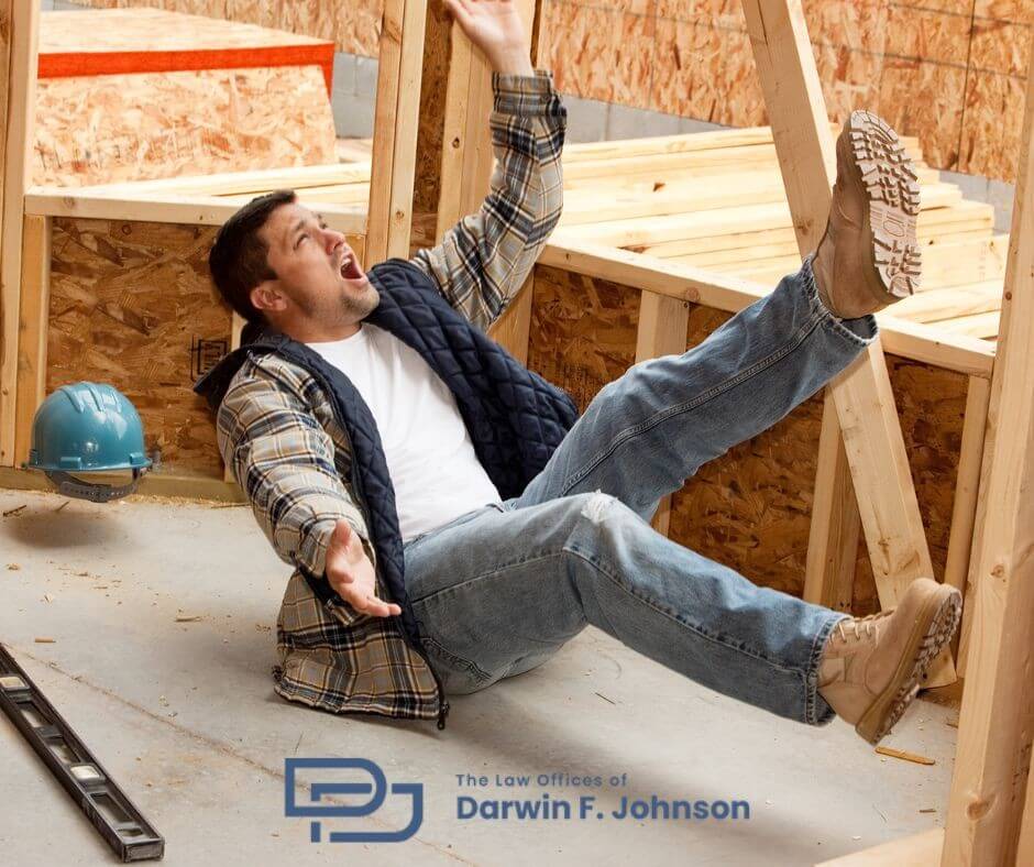 A man wearing jeans and a plaid shirt falls backward at a construction site, with tools and a hard hat nearby. A law office logo is visible in the lower part of the image.