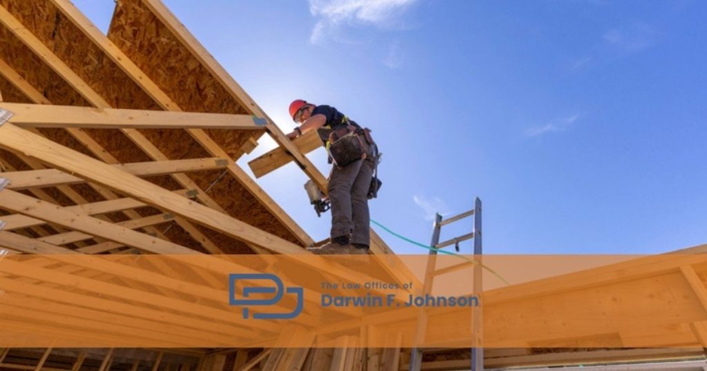 Construction worker wearing safety gear stands on a wooden roof frame under a blue sky, with a ladder nearby. "The Law Office of Darwin F. Johnson" logo is overlaid.