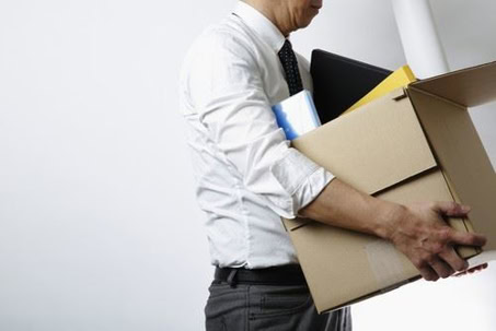 A man in business attire carries a cardboard box filled with office supplies and personal items.