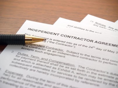 A pen rests on top of an independent contractor agreement document lying on a wooden surface.