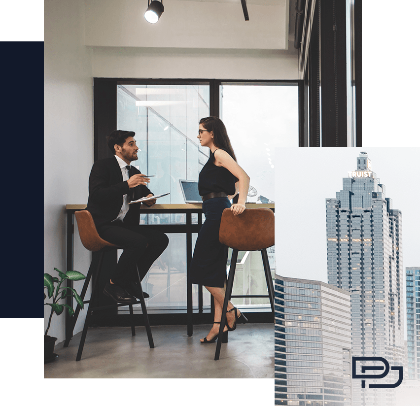 A man in a suit and a woman in business attire talk at a high table in a modern office with large windows; an image of a tall city skyscraper is overlaid in the corner.