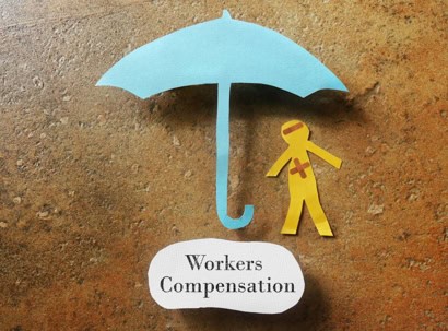 Paper cutouts of a blue umbrella and an injured worker are shown above the words "Workers Compensation" on a brown textured background.