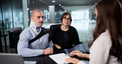 injured man wearing neck brace and arm sling meeting with legal professional
