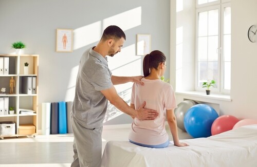 physical therapist examining female patient's back during rehabilitation session